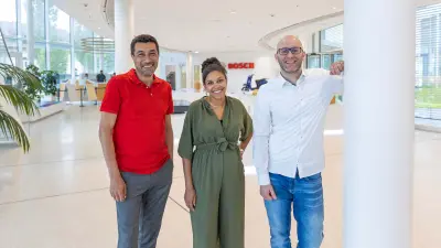 Mustafa (links), Sarah (Mitte) und Simon (rechts) stehen im Foyer des IT Campus' Stuttgart-Feuerbach und lächeln in die Kamera.