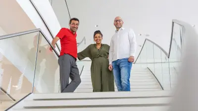 Mustafa (links), Sarah (Mitte) und Simon (rechts) stehen auf der Treppe im Foyer des IT-Campus' und lachen.