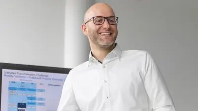 Simon lacht einen Kollegen an. Er ist bis zum Oberkörper zu sehen.