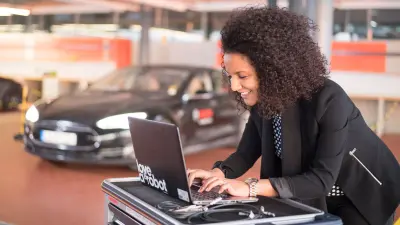 Frau arbeitet an Laptop neben Auto